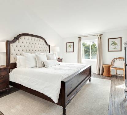Sink into crisp white linens and a plush tufted headboard in your serene bedroom, complete with warm wood furnishings and tropical artwork.