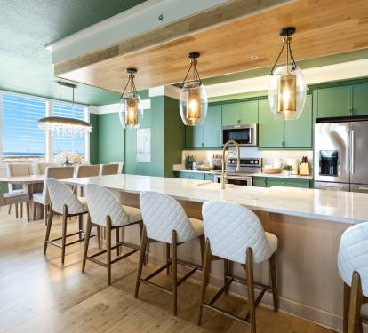 Your modern kitchen features sleek green cabinets, marble countertops, and stylish pendant lighting perfect for preparing meals and entertaining.
