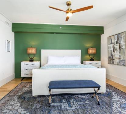 Your serene bedroom features a plush white bed against a soothing green accent wall, with warm bedside lighting and modern ceiling fan for your comfort.