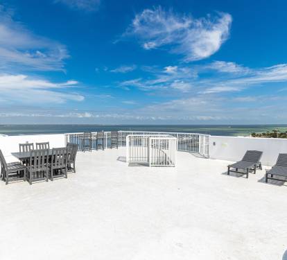 Expansive rooftop terrace featuring dining and lounging areas with panoramic ocean views under brilliant blue skies.