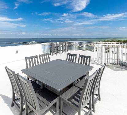 Expansive rooftop terrace with dining table overlooking waterfront views, perfect for outdoor meals with ocean breeze.