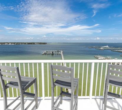 Sweeping waterfront panorama from an elevated balcony showcasing marina views, docks, and pristine coastal waters under expansive blue skies.