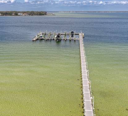 Aerial view showcasing a wooden pier extending into crystal-clear waters, part of the coastal area surrounding the property.