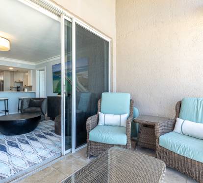 Relax on your private balcony with comfy wicker chairs and turquoise cushions, overlooking the modern living space inside through sliding glass doors.