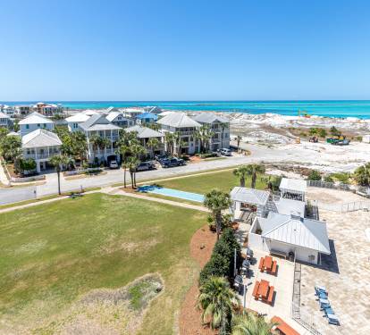 Stunning aerial view of beachfront vacation homes with pristine white sand beaches and turquoise waters stretching to the horizon.