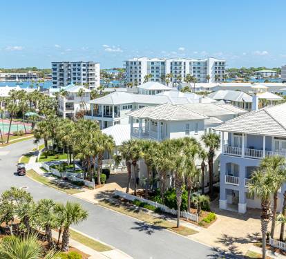 Aerial view of a coastal resort community featuring white buildings, palm trees, and nearby waterfront amenities.