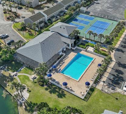 Aerial view showcasing the property's impressive amenities including swimming pool, tennis courts, and clubhouse surrounded by palm trees and parking areas.