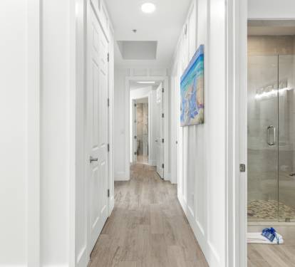 Walk through your bright, modern hallway where coastal artwork creates a calming atmosphere, leading to your private ensuite bathroom with a luxurious glass shower.