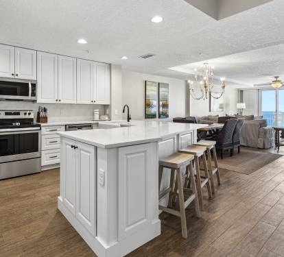 Your spacious kitchen flows into the open living area, featuring white cabinetry, modern appliances, and island seating with stunning ocean views.