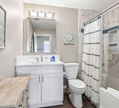 Step into your private bathroom featuring marble-look tiles, crisp white vanity, and coastal artwork that creates a spa-like retreat for your getaway.