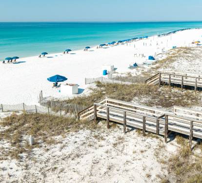 Pristine white sand beach with crystal-clear turquoise waters and wooden boardwalk providing easy access to this Gulf Coast paradise.
