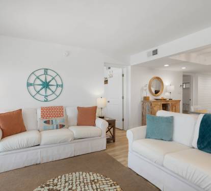 Sink into plush white sofas adorned with coastal-inspired pillows, where nautical charm meets modern comfort in your bright, airy retreat.