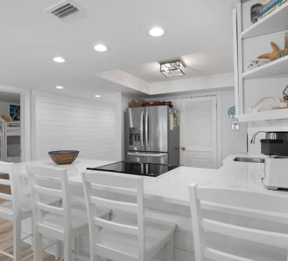 Your modern kitchen invites culinary adventures with pristine white countertops, stainless steel appliances, and a breakfast bar perfect for morning coffee.