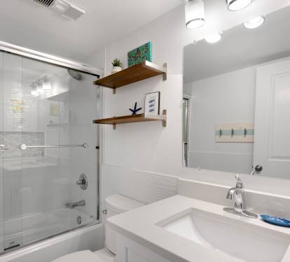 Unwind in your pristine bathroom featuring a glass-enclosed tub-shower combo and stylish vanity with thoughtful coastal touches.