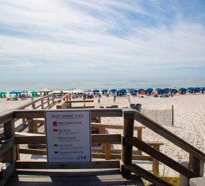 Sandy beach with colorful umbrellas and clear safety signage provides a welcoming coastal destination for visitors.