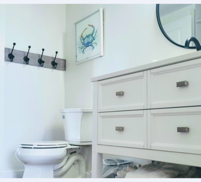 Your bright bathroom features coastal charm with a vanity offering ample storage and convenient wall hooks for your belongings.