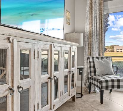 Coastal-inspired living space with stylish décor, a large flatscreen TV, comfortable seating, and peaceful lake views.