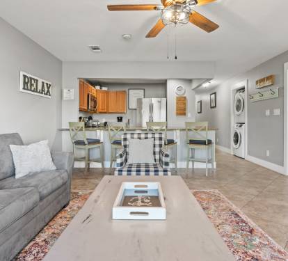 Open living space with coastal décor, comfortable seating, and a full kitchen designed for easy vacation living.
