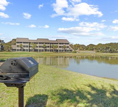 Community charcoal grilling area with peaceful golf course and lake views—perfect for outdoor meals after a beach day.