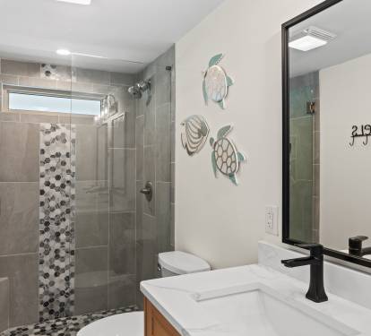 Step into your spa-like bathroom where the mosaic-tiled walk-in shower and coastal turtle artwork create a serene retreat.