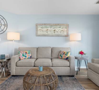 Charming coastal living room with a comfy sofa, beachy artwork, rattan coffee table, and soft blue walls—perfect for unwinding after a sunny day at the beach.