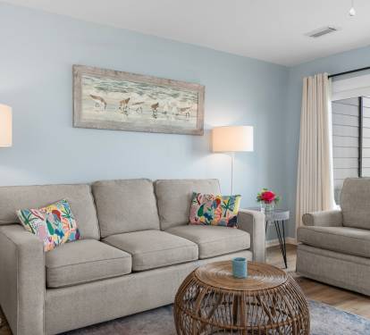 Cozy coastal living room with a plush sofa, tropical accent pillows, rattan coffee table, and beach-themed wall art—perfect for relaxing after a day in the sun.
