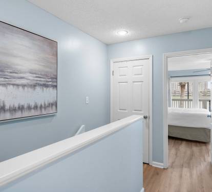 Upstairs hallway with soft coastal tones and wood flooring leads to serene bedrooms—creating a calm transition between living and sleeping spaces.
