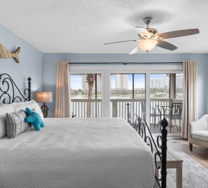 Wake up to stunning lake views in the airy primary bedroom featuring a plush king bed, soft coastal tones, and direct access to a private balcony for peaceful mornings or sunset unwinding.