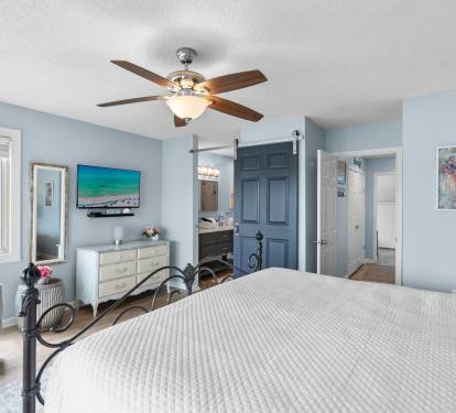 Primary bedroom features a king bed, wide-screen TV, and en-suite bath with a stylish barn door—combining comfort, privacy, and coastal charm in one relaxing space.