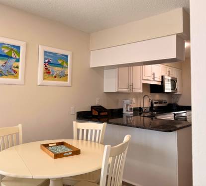 Your bright, fully equipped kitchen opens to a cozy dining nook where beachy artwork sets a relaxed, coastal mood for meals together.