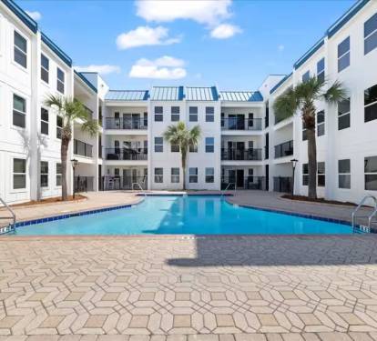 Beautiful resort-style courtyard pool surrounded by palms and lounge seating—your private oasis near the beach.