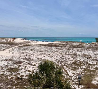A coastal property location features sandy terrain, native vegetation, and stunning turquoise waters visible from the surrounding area.