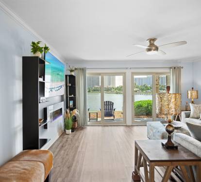 Spacious lakefront living room with modern decor, large glass doors, electric fireplace, and LVP wood floors. Features patio access and stunning water views.