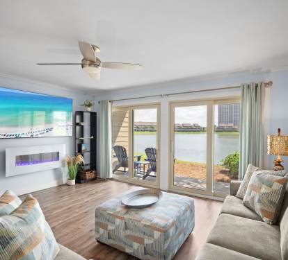 Bright lakefront living room with sliding glass doors, modern fireplace, cozy sectional, and LVP wood floors. Relaxed, coastal vibe with patio access and scenic views.
