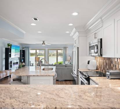 Open-concept kitchen and living area with granite countertops, stainless steel appliances, and custom tile backsplash. Bright and airy with lake views and coastal-inspired decor throughout.
