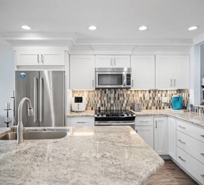 Sleek kitchen with granite countertops, stainless steel appliances, white cabinetry, and a bold tile backsplash. Bright, modern, and fully equipped for cooking and entertaining.