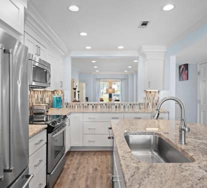Contemporary kitchen with granite countertops, stainless steel appliances, white cabinetry, and a stylish backsplash. Features an open layout with bar seating.