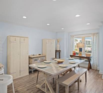 Airy dining space with a modern table, bench seating, and LVP wood floors. Light-toned furnishings and a window bring in natural light and a coastal charm. The table in front of the window converts to a desk for a laptop-friendly space.