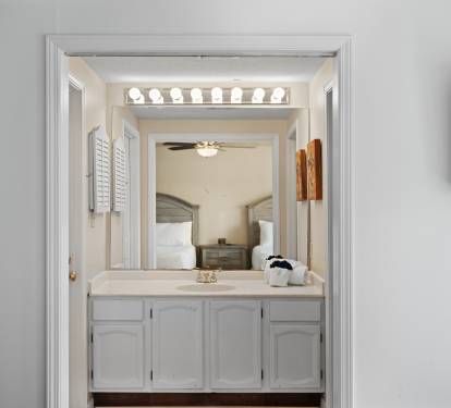Guest ensuite vanity area with wide countertop, large mirror, bright Hollywood-style lighting, and white cabinetry. Clean and functional, with direct access to the bedroom.