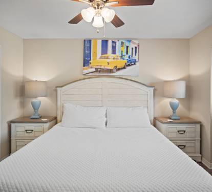 Cozy primary bedroom with a king bed, matching nightstands, and soft lighting from bedside lamps. Features a ceiling fan, neutral walls, and vibrant artwork for a warm, inviting atmosphere.