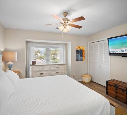 Includes a wall-mounted TV, neutral tones, and warm wood flooring for a relaxed retreat.