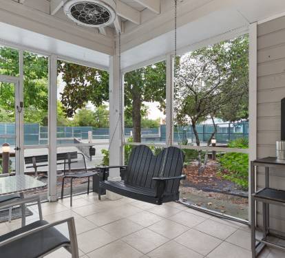 Unwind on the screened-in patio with a porch swing, cozy seating, and views of the nearby tennis courts.