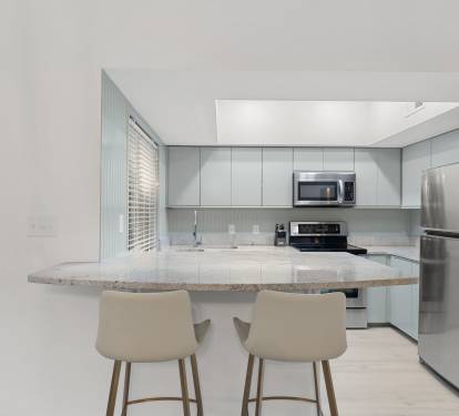This modern kitchen features sleek appliances, soft coastal tones, and a bar perfect for morning coffee.