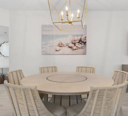 Gather in this coastal-chic dining space featuring a round wood table, woven chairs, and elegant lighting.