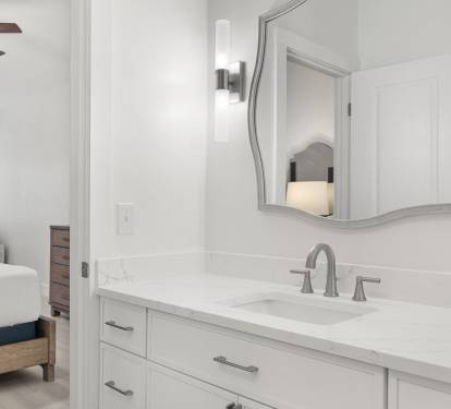 The en-suite bathroom features a sleek white vanity, modern fixtures, and a bright, clean coastal design.