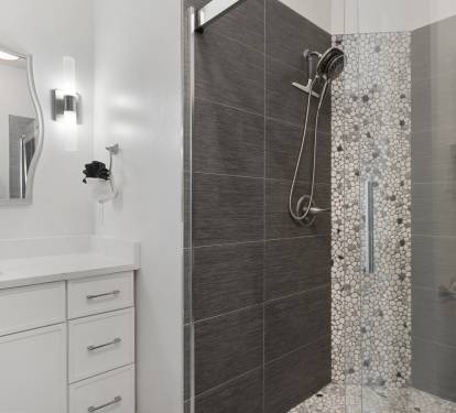 The en-suite bathroom showcases a custom walk-in shower with dark tile, pebble accents, and modern finishes.