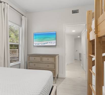 The guest room includes a queen bed, twin bunks, a flat-screen TV, and soft natural light for a restful stay.