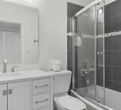 This stylish guest bathroom offers a clean white vanity, modern fixtures, and a tub/shower combo with dark tile and mosaic accent trim.