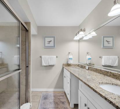 Coastal-inspired bathroom featuring a walk-in shower and dual vanity. Soft lighting and fresh towels await after your day exploring.