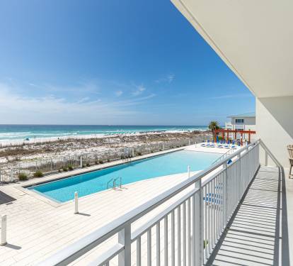 Stunning beachfront balcony with panoramic ocean views, pool access, and outdoor seating overlooking pristine sandy shores.
